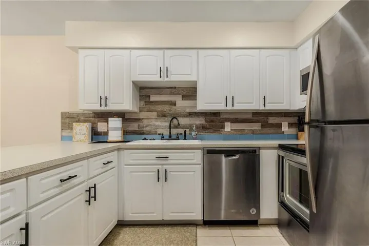 Kitchen with white cabinetry, light tile patterned floors, appliances with stainless steel finishes, decorative backsplash, and sink