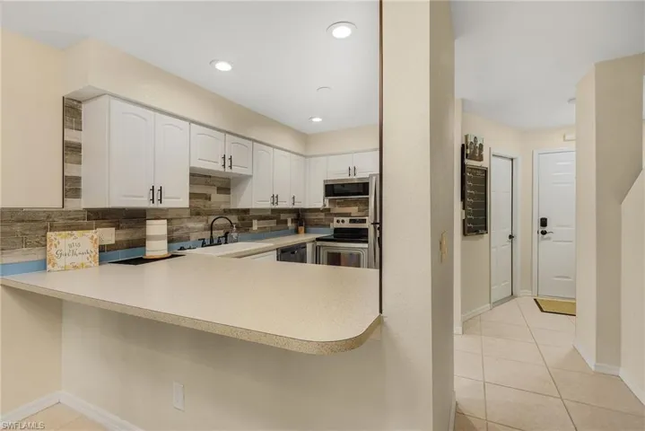 Kitchen featuring white cabinetry, light tile patterned floors, backsplash, appliances with stainless steel finishes, and sink