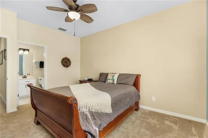 Bedroom with ceiling fan, connected bathroom, and light colored carpet