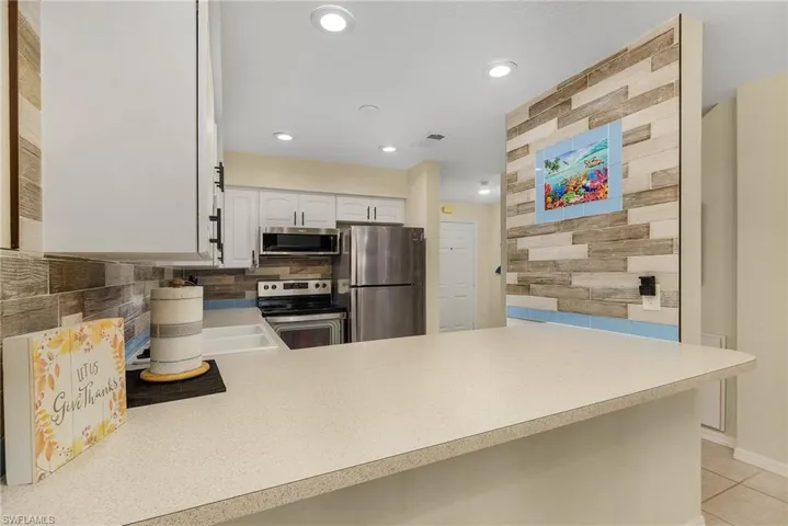 Kitchen featuring stainless steel appliances, kitchen peninsula, light tile patterned floors, decorative backsplash, and white cabinetry