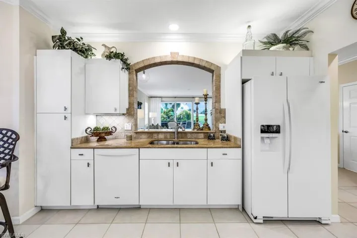Kitchen featuring white appliances, white cabinetry, backsplash, light tile patterned floors, and sink