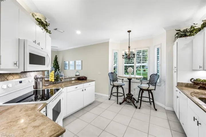 Kitchen with white appliances, light tile patterned floors, ornamental molding, white cabinetry, and a chandelier
