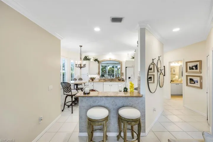 Kitchen featuring kitchen peninsula, ornamental molding, light tile patterned floors, white cabinets, and white fridge