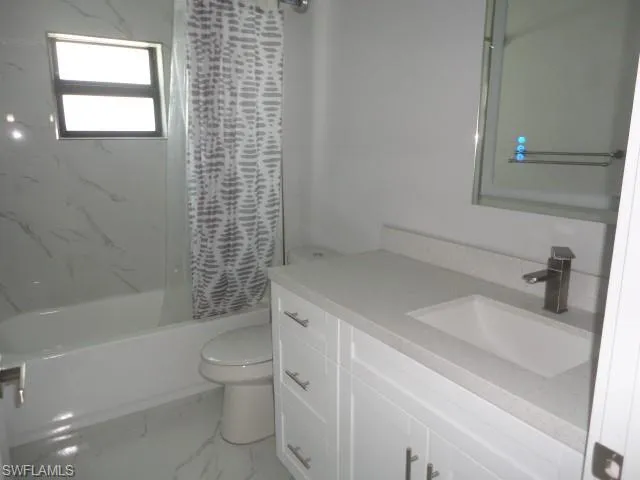 Bathroom with toilet, marble look tile flooring, shower / bathtub combination with curtain, and vanity