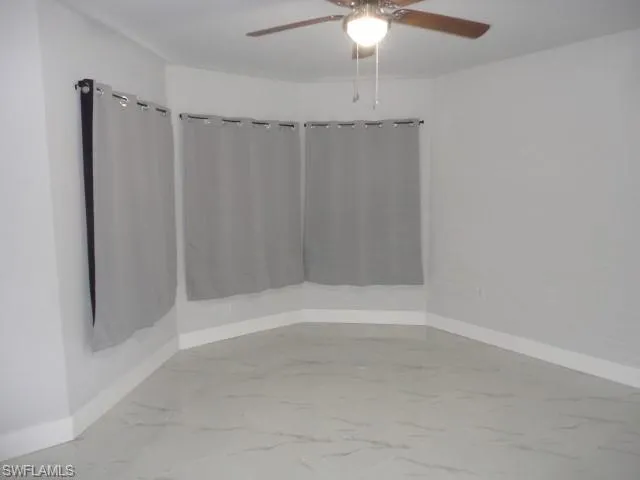 Empty room featuring a ceiling fan, baseboards, and marble finish flooring