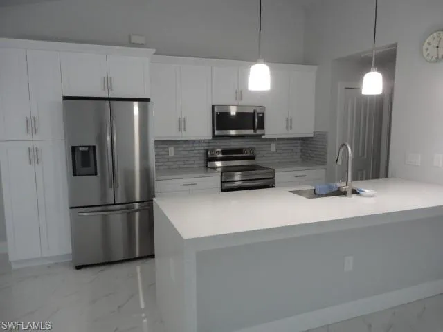Kitchen featuring stainless steel appliances, light marble finish floors, a sink, tasteful backsplash, and white cabinets