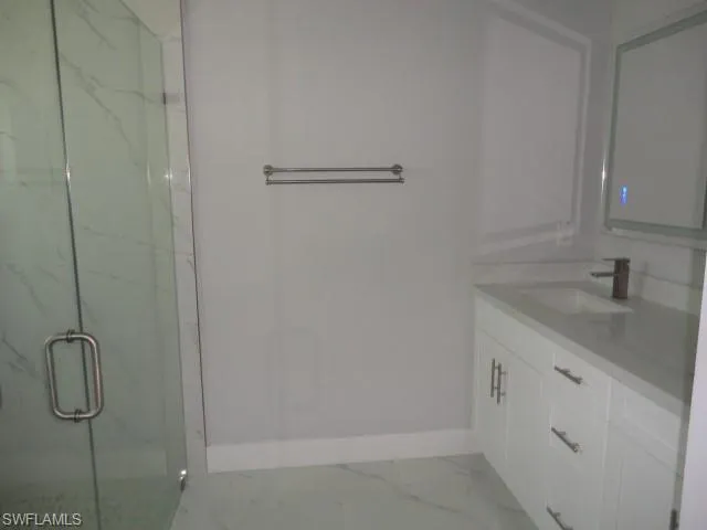 Bathroom featuring baseboards, marble look tile flooring, a marble finish shower, and vanity