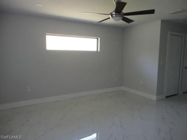 Spare room featuring baseboards, marble look tiles, and a ceiling fan