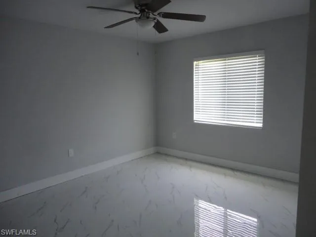 Unfurnished room featuring baseboards, a ceiling fan, and light marble finish floors