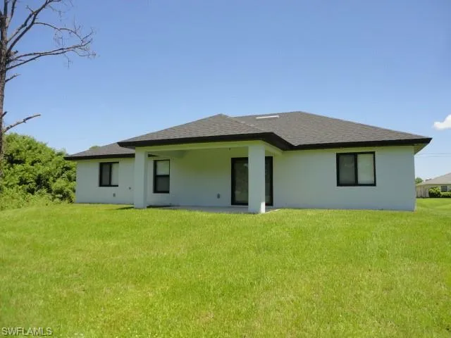 Back of house with a lawn, stucco siding, and a shingled roof