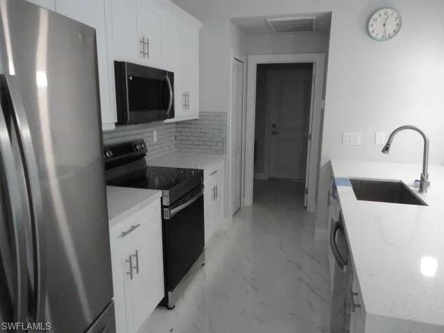 Kitchen featuring freestanding refrigerator, black electric range, a sink, light marble finish floors, and decorative backsplash