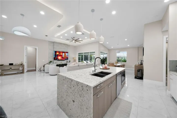 Kitchen with open floor plan, hanging light fixtures, light stone counters, an island with sink, and recessed lighting