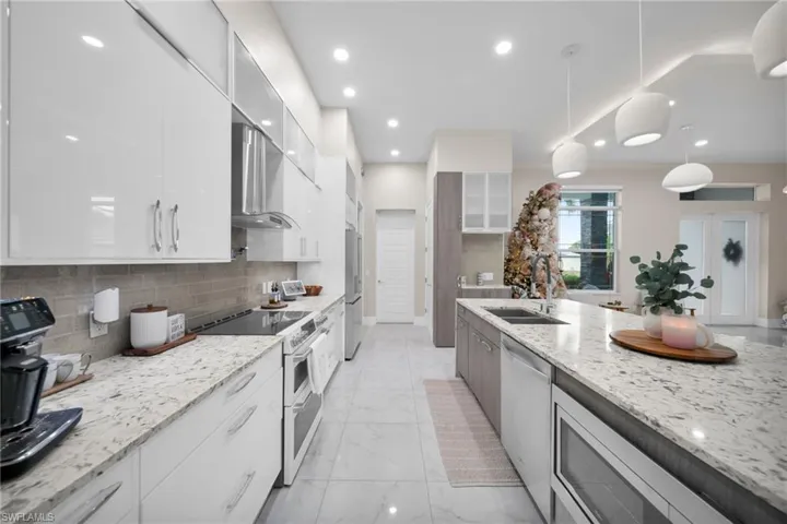Kitchen with white cabinets, modern cabinets, stainless steel appliances, light stone countertops, and recessed lighting