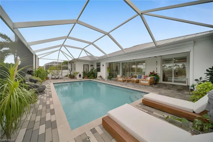 Outdoor pool with glass enclosure, a sunroom, a patio area, and an outdoor living space