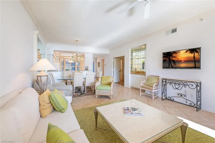 Living area featuring light tile patterned floors, a chandelier, crown molding, and a ceiling fan