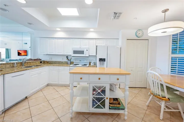 Kitchen with white cabinets, white appliances, hanging light fixtures, a tray ceiling, and recessed lighting