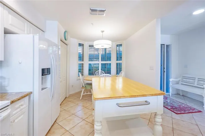 Kitchen featuring white cabinetry, white fridge with ice dispenser, decorative light fixtures, and light tile patterned flooring