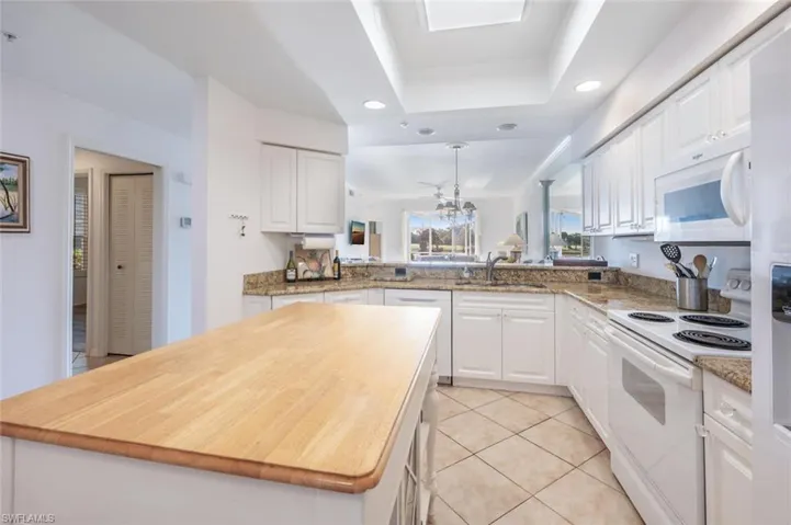 Kitchen featuring white appliances, white cabinets, a kitchen island, a tray ceiling, and recessed lighting