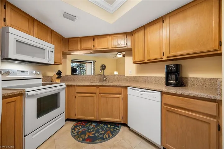 Kitchen with white appliances, light tile patterned flooring, a ceiling fan, and light stone countertops