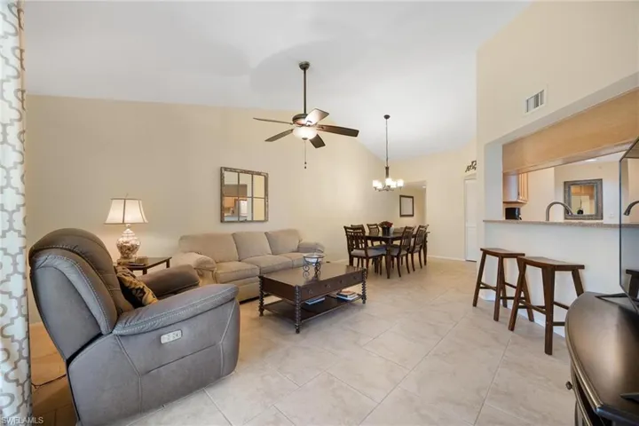 Living room with a ceiling fan, light tile patterned floors, high vaulted ceiling, and a chandelier