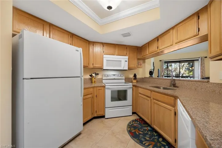Kitchen with white appliances, light tile patterned floors, crown molding, a raised ceiling, and light stone counters