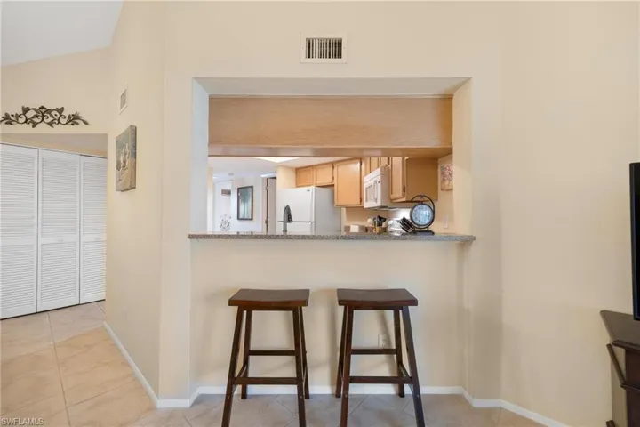 Kitchen featuring a breakfast bar area, white appliances, light tile patterned floors, light stone countertops, and light brown cabinets