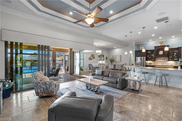 Living room featuring light tile flooring, ceiling fan, a raised ceiling, and crown molding