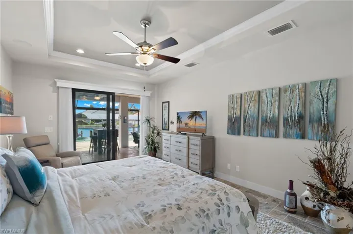 Tiled bedroom featuring ceiling fan, a tray ceiling, and access to exterior