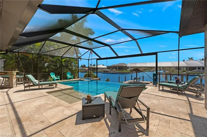 View of swimming pool with a patio, glass enclosure, and a water view
