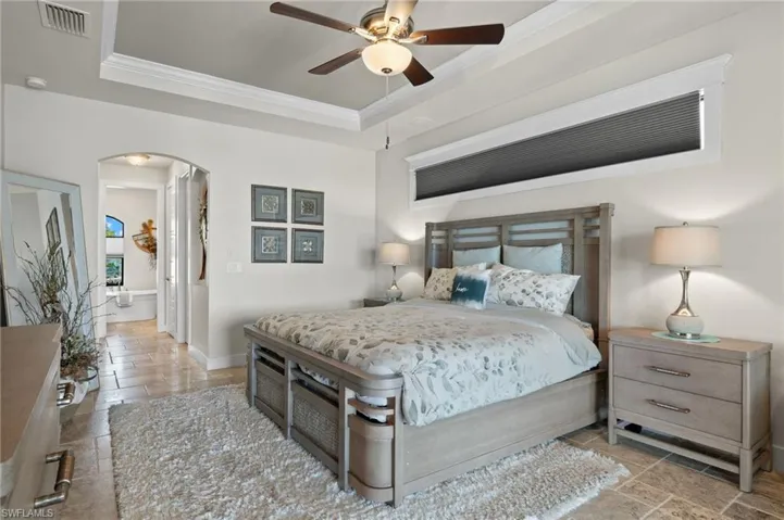 Tiled bedroom featuring ceiling fan, a raised ceiling, and ornamental molding