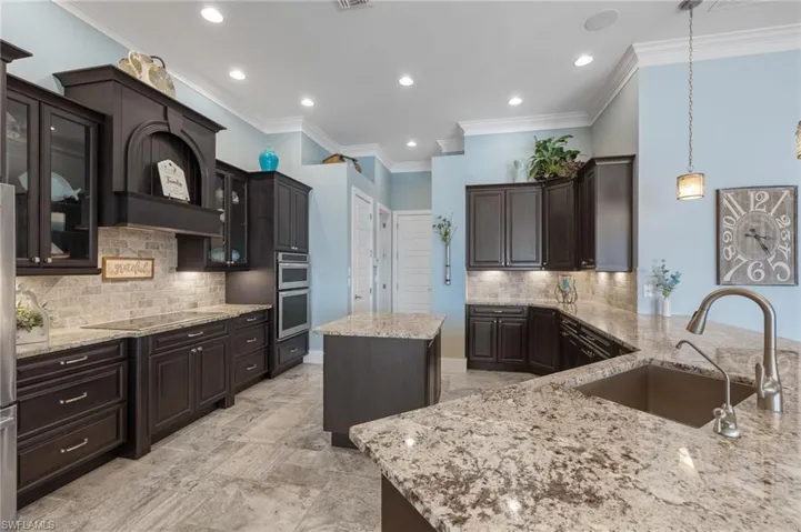 Kitchen with decorative light fixtures, a kitchen island, backsplash, black electric cooktop, and sink