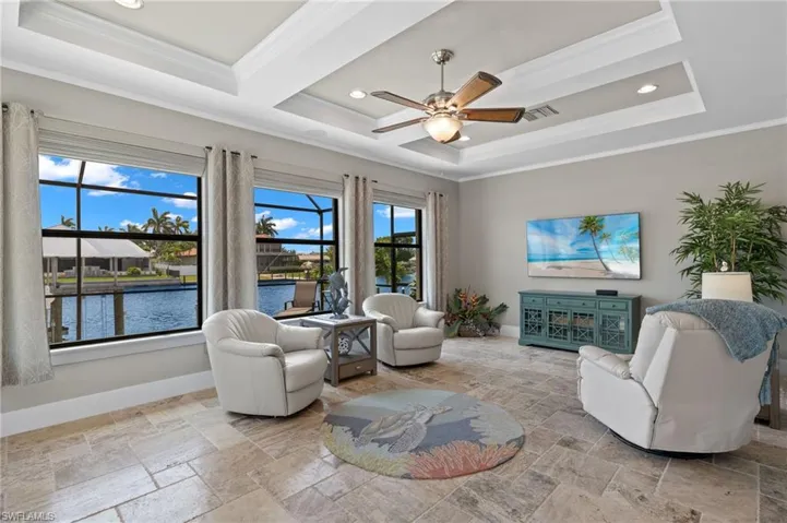 Tiled living room featuring ornamental molding, ceiling fan, a water view, and a raised ceiling