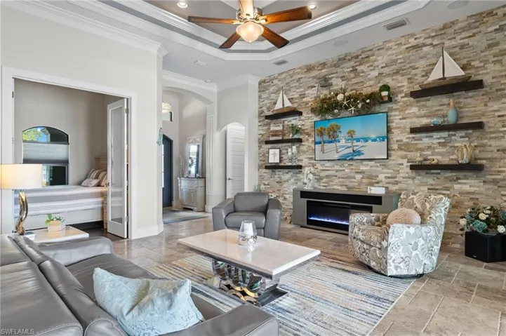 Living room with a tray ceiling, tile floors, crown molding, and ceiling fan