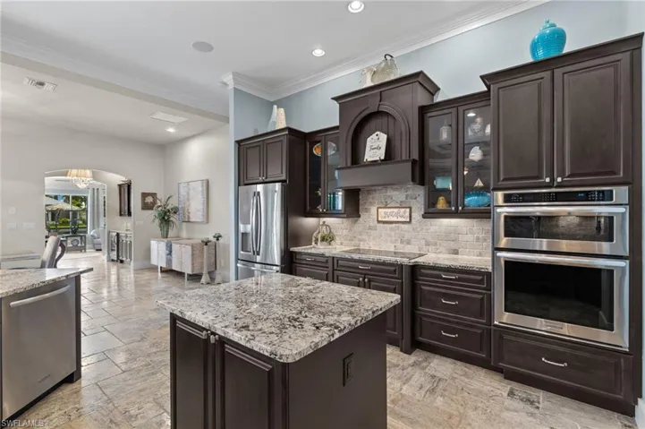 Kitchen featuring a kitchen island, appliances with stainless steel finishes, dark brown cabinetry, tasteful backsplash, and light tile flooring
