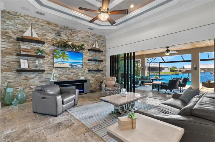 Living room featuring a tray ceiling, a water view, ceiling fan, and tile floors