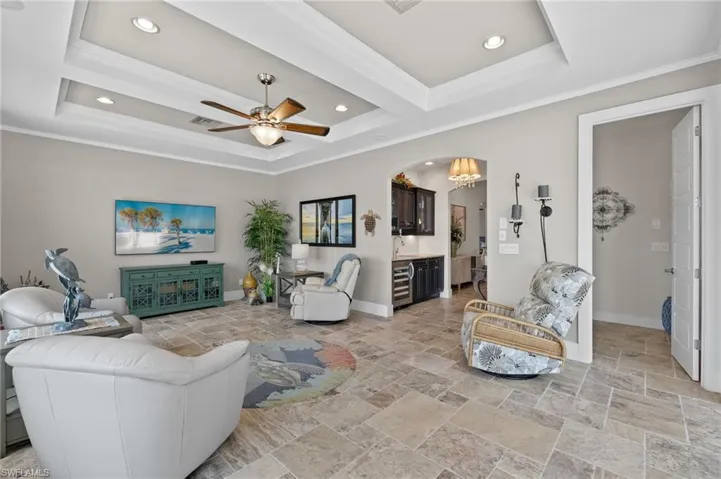 Tiled living room featuring crown molding, a raised ceiling, and ceiling fan with notable chandelier