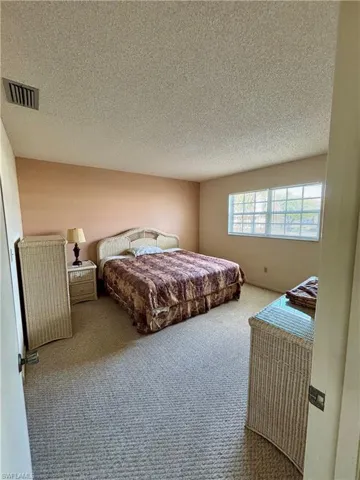 Bedroom with a textured ceiling, carpet flooring, and visible vents