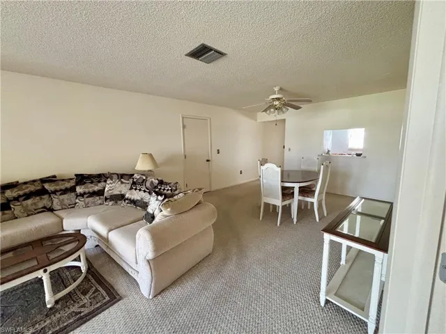 Carpeted living area with ceiling fan, a textured ceiling, and visible vents