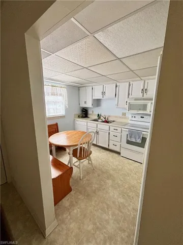 Kitchen with white appliances, light countertops, light floors, white cabinetry, and a sink