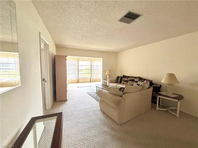 Living area with carpet floors, visible vents, and a textured ceiling