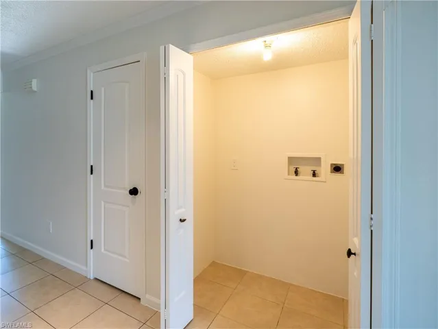 Laundry room with electric dryer hookup, crown molding, light tile floors, washer hookup, and a textured ceiling