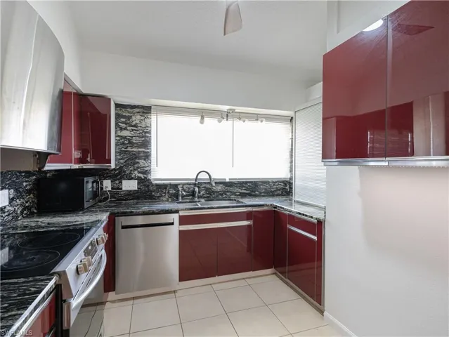 Kitchen featuring appliances with stainless steel finishes, sink, light tile floors, and dark stone counters