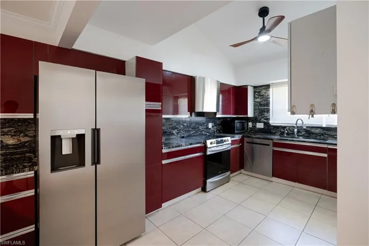 Kitchen with stainless steel appliances, backsplash, sink, ceiling fan, and light tile floors