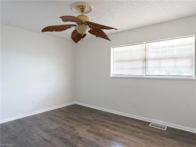 Unfurnished room with dark hardwood / wood-style floors, ceiling fan, and a textured ceiling