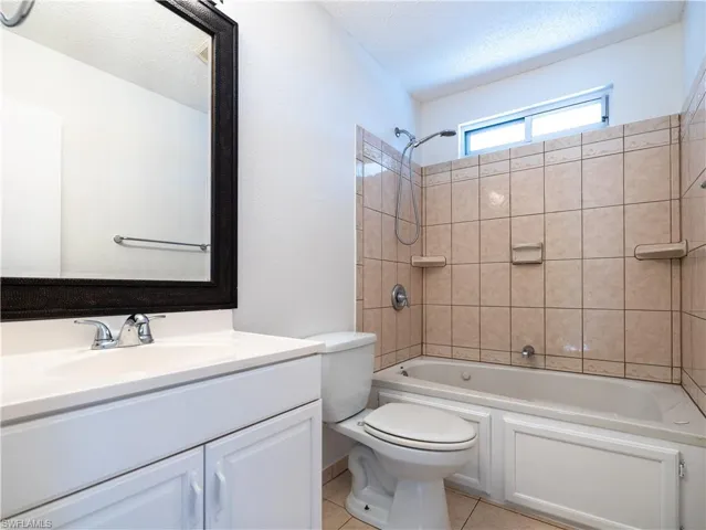 Full bathroom with tile flooring, tiled shower / bath, a textured ceiling, toilet, and vanity