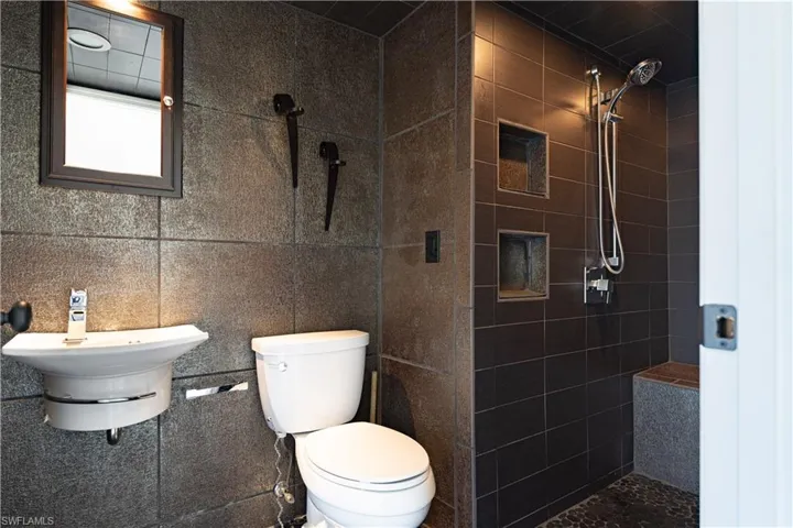 Bathroom with a tile shower, tile walls, and toilet