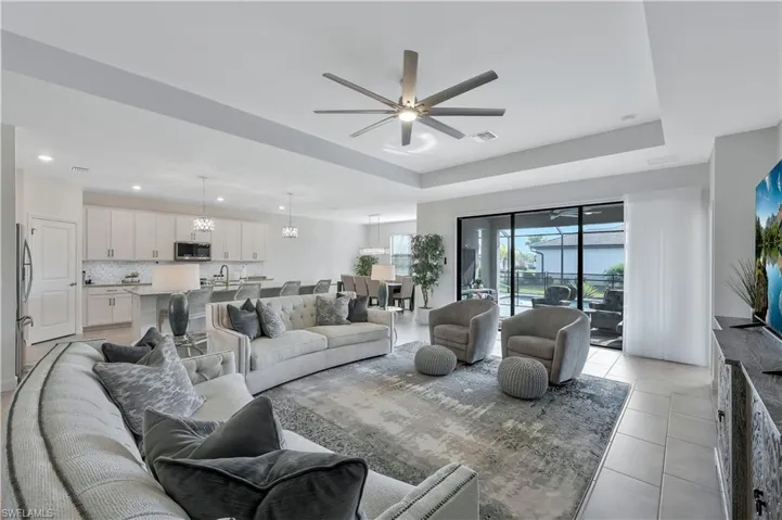 Living area with a tray ceiling, light tile patterned floors, visible vents, ceiling fan, and recessed lighting
