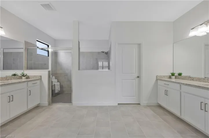 Full bathroom featuring baseboards, a tile shower, visible vents, and two vanities