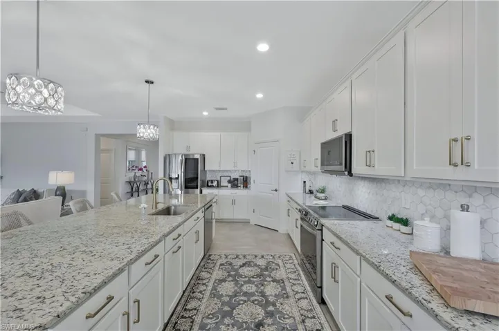 Kitchen with a sink, white cabinetry, appliances with stainless steel finishes, decorative backsplash, and an inviting chandelier