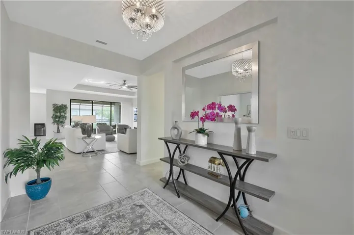 Hallway with a tray ceiling, tile patterned floors, visible vents, and a chandelier